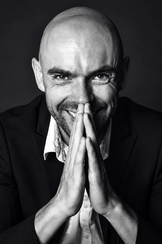 Portrait rapproché en noir et blanc d’un homme souriant, les mains jointes devant le visage — séance Leadership à Lyon.